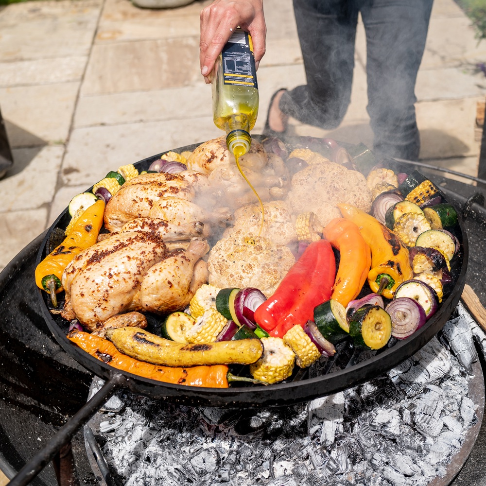 Plain Jane Fire Pit with Swing Arm - 50cm, 60cm and 70cm Variations. Lifestyle Image with Food Cooking on the Swing Arm